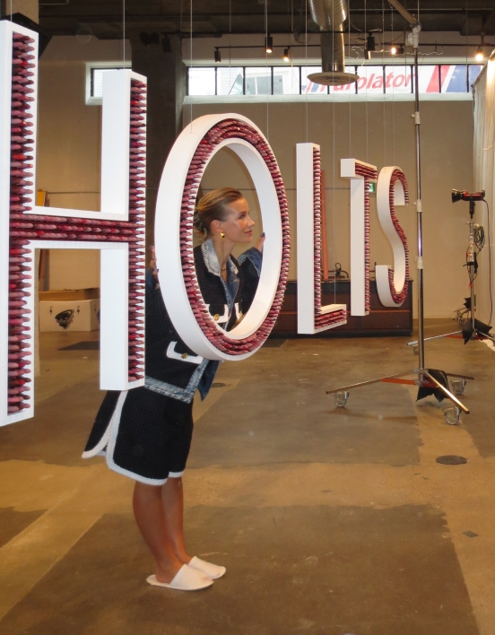 Emy-Jade poking her head through the giant “O” in “HOLTS” made up of lipsticks.