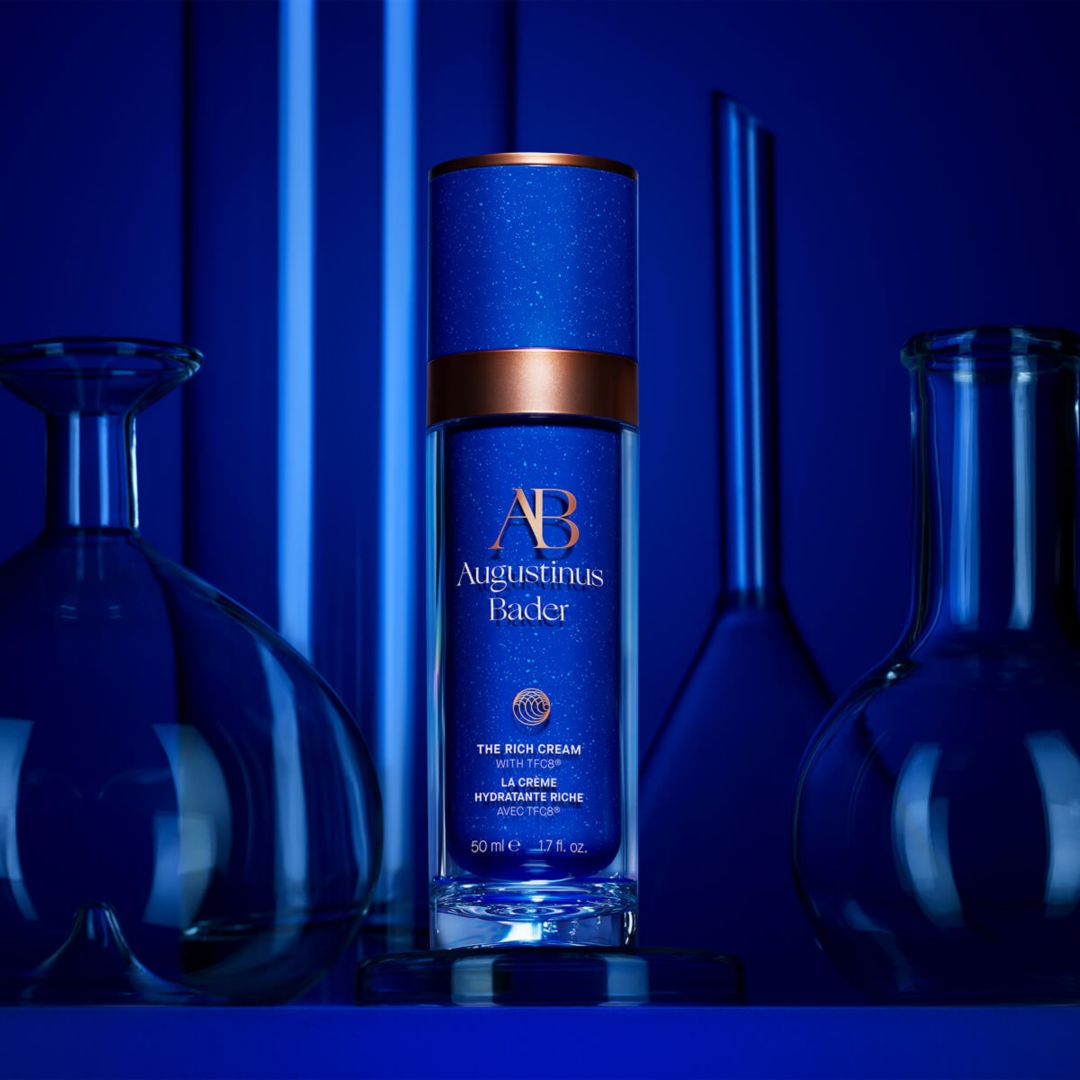 A Blue Augustinus Bader facial cream sitting infront of a blue soaked background