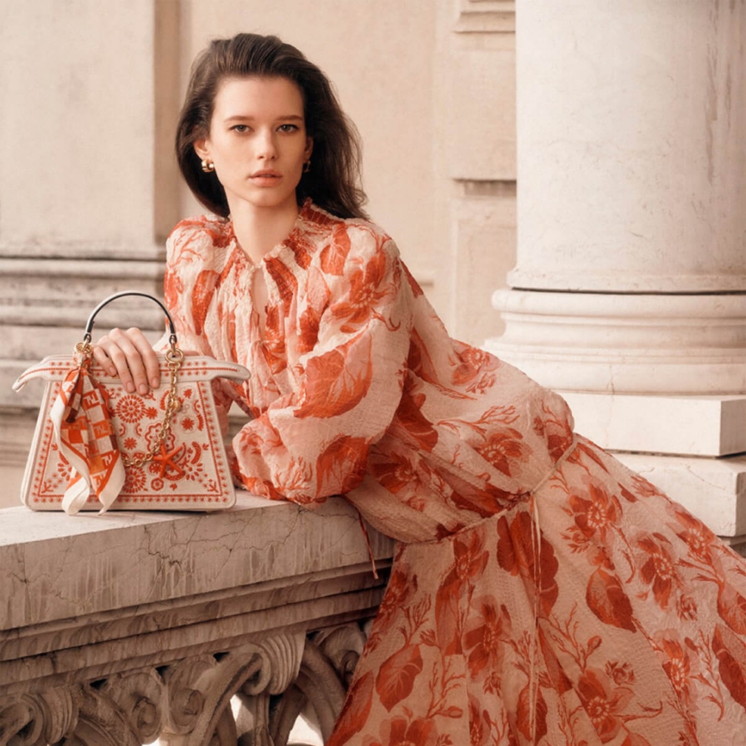 A model dressed in an orange floral dress with a stunning Fendi bag.