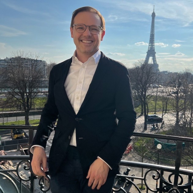 Sebastian standing on a balcony in Paris with the Eiffel Tower in the background.