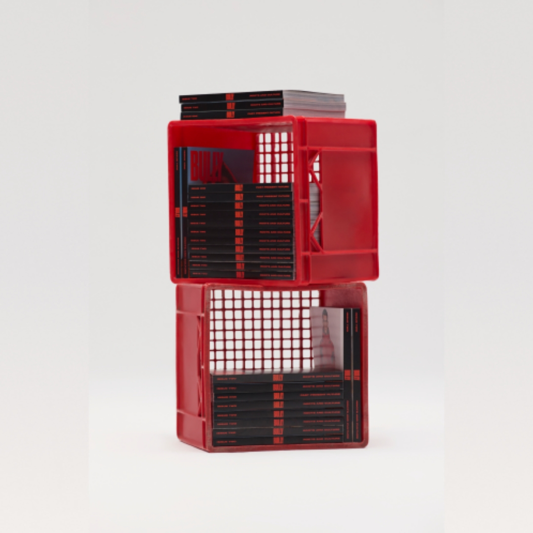 Two red crates are stacked atop each other, filled with BULLY magazines with black spines.