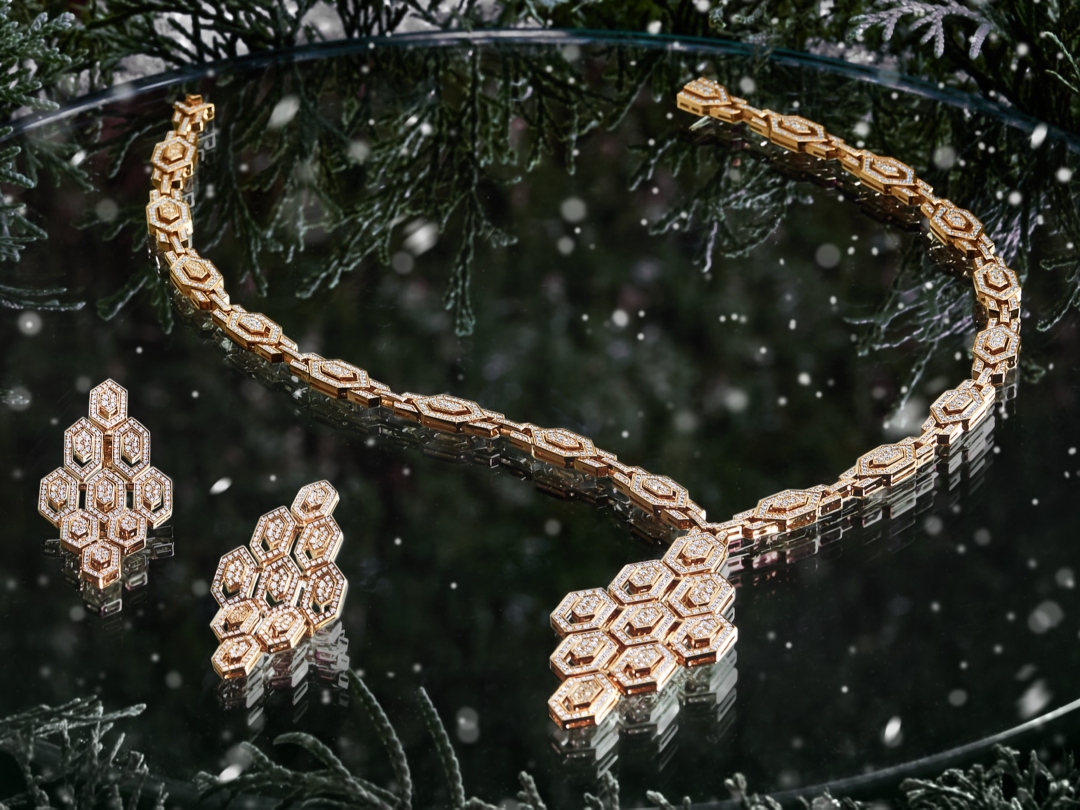 A pair of gold earrings with diamonds and a diamond necklace placed on a reflected surface surrounded by festive green foliage.