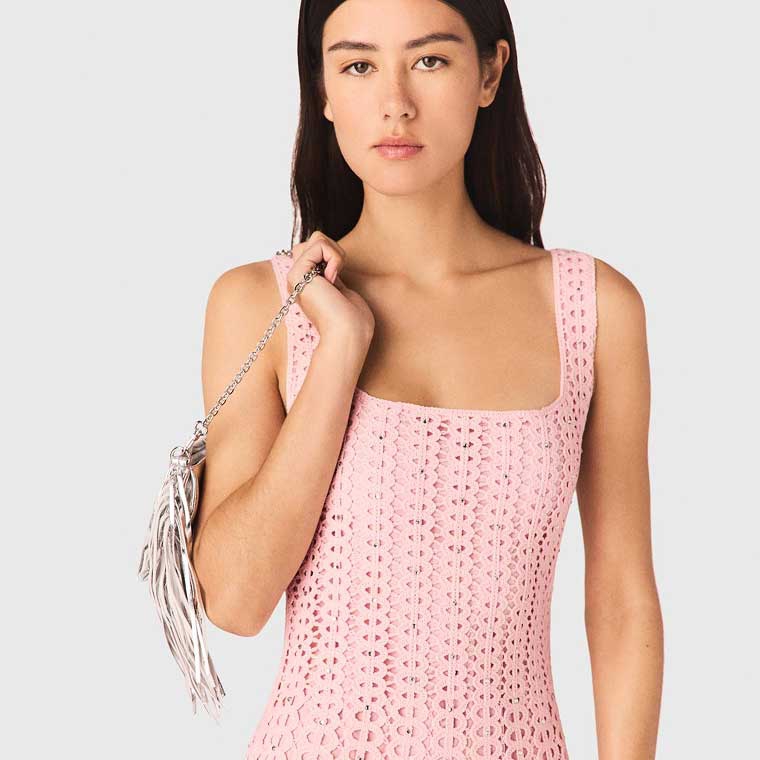 A model wearing a crocheted pink mini dress and holding a silver purse.