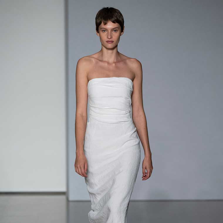 A model walking down a runway wearing a strapless white dress.