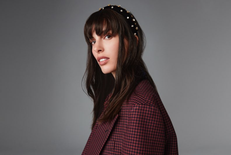A model in a plum coat wearing a pearl encrusted headband for the holidays