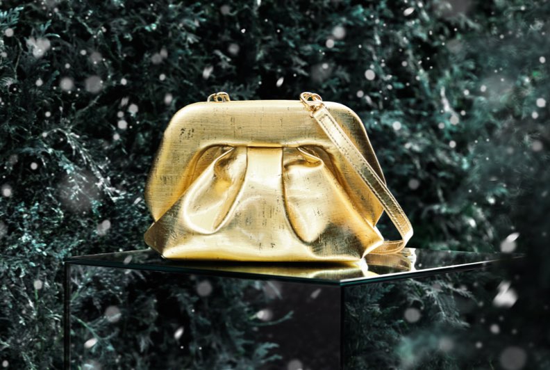 A gold clutch bag sitting on top of a mirrored surface in front a lush green background