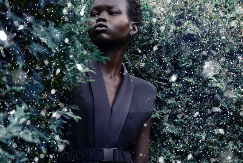 A model dressed in a black sleeveless blazer accessorized with leather gloves and a red bag