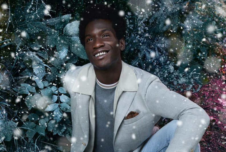 Model weaing a grey blazer sitting and smiling among foliage