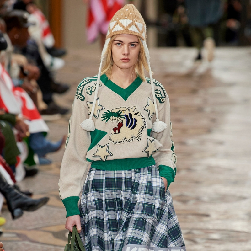 A model wearing a sweater with a graphic print and a plaid skirt.