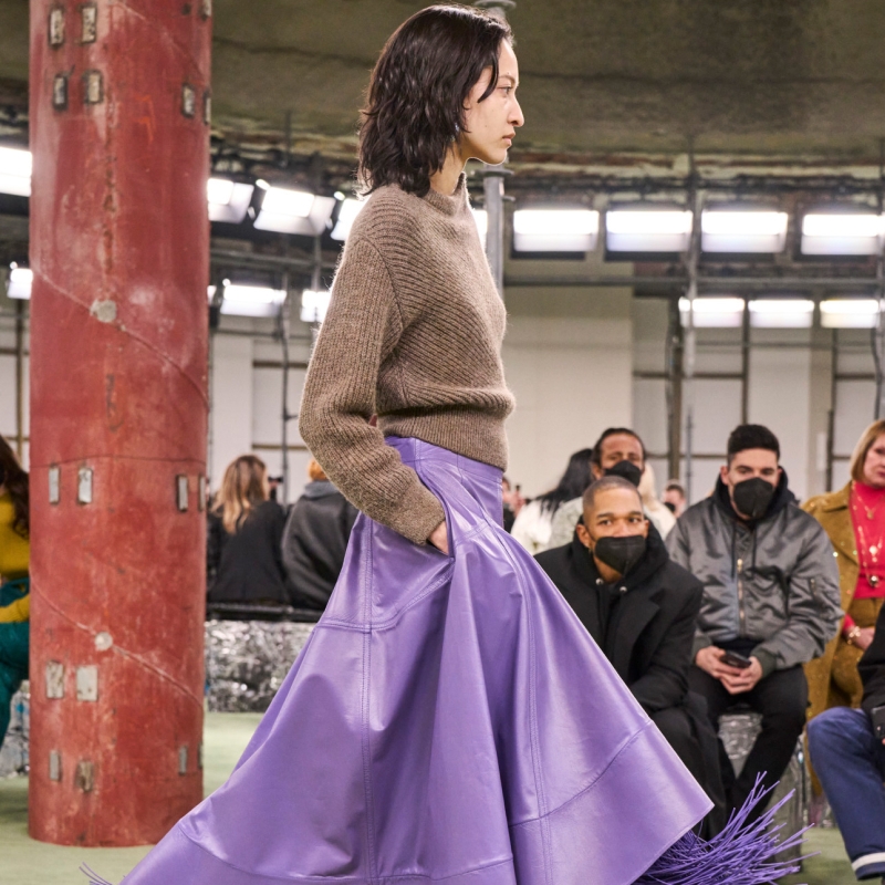 A model wearing a camel sweater with a purple leather A-line skirt.