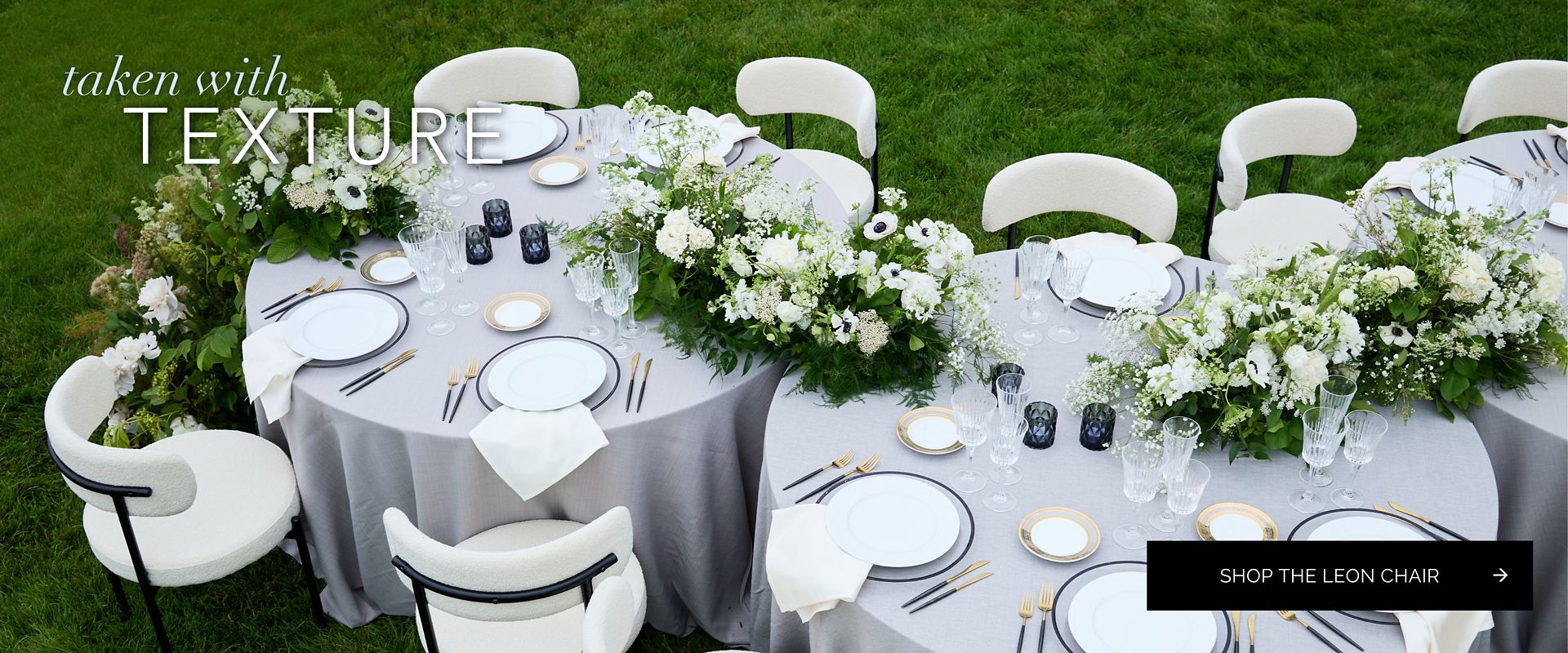 Outdoor dining setup showing the Leon Chair in ivory bouclé surrounding round tables set with elegant white and gold dinnerware and white floral runners.