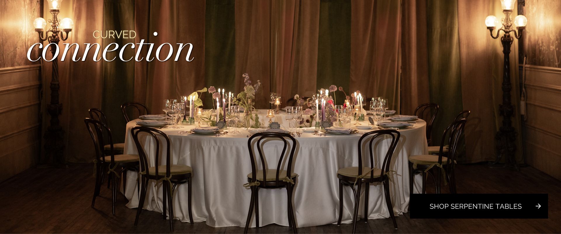 Candlelit serpentine table setting with white linen and bentwood chairs.