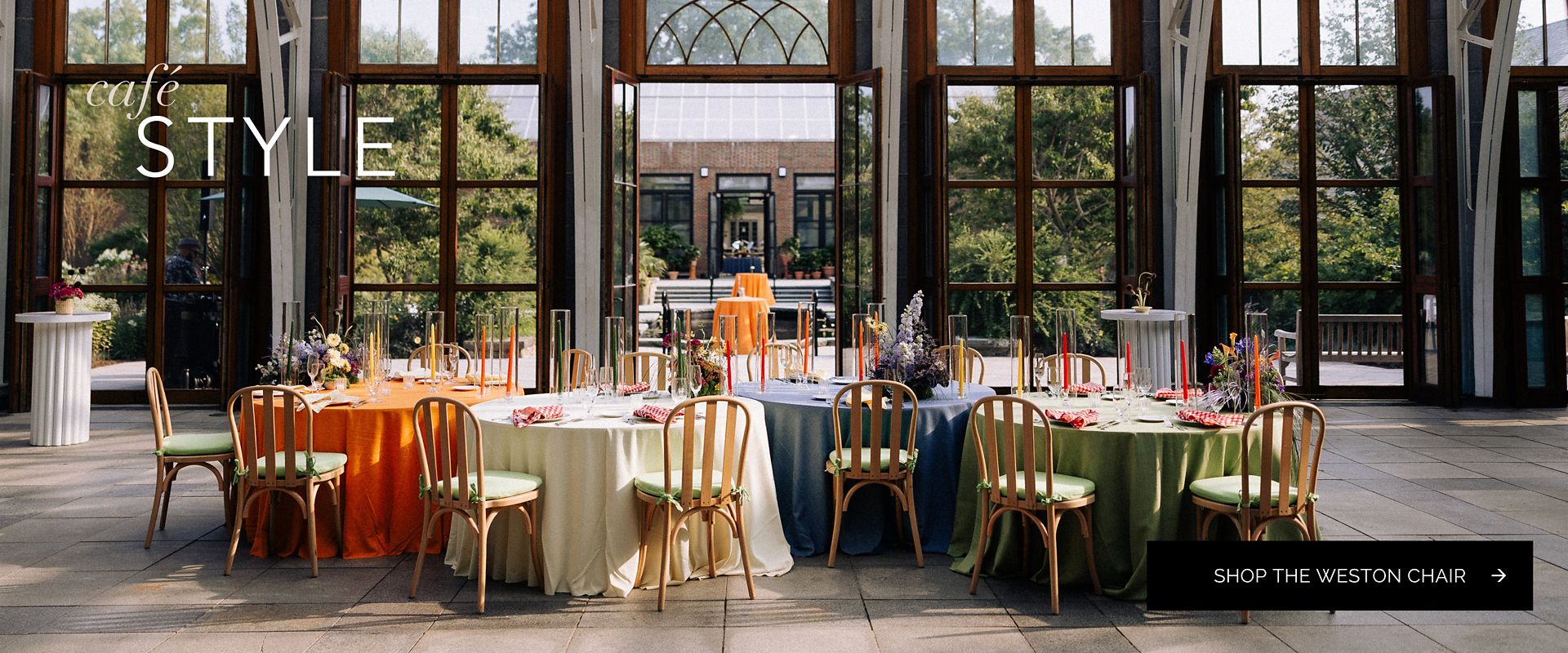 Weston wood chairs with green cushions surrounding colorful linen-covered tables in a sunlit garden venue.