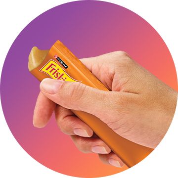 hand holding a tube of friskies lil' lickables cat treat and squeezing it