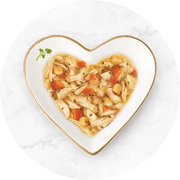 white heart shaped bowl with a gold rim filled with chicken and carrot cat food topper