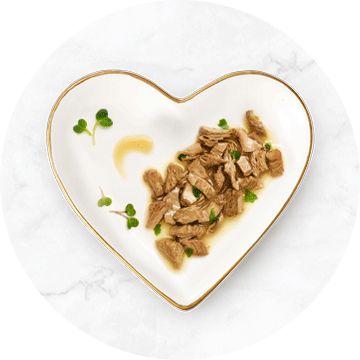 white heart shaped bowl with a gold rim filled with chunks of wet cat food in gravy