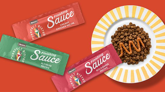 Purrfect Bistro finishing sauce packaging next to a plate of dry cat food with sauce on top