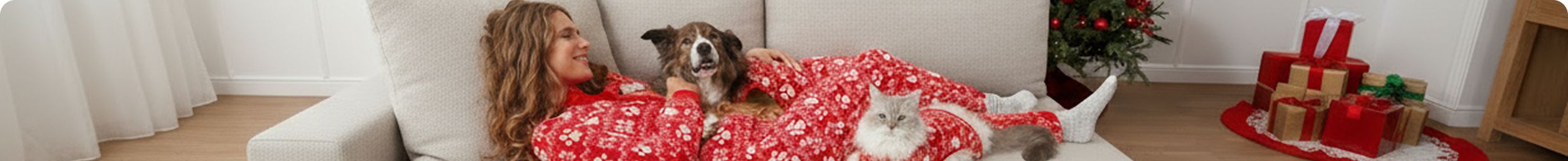 Woman wearing festive pajamas laying on a couch with a dog & cat