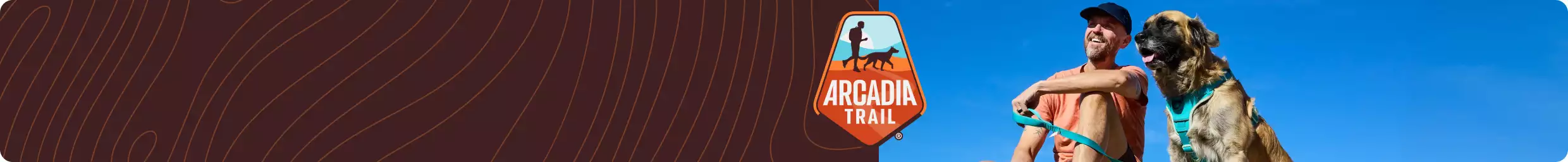 Pet parent & dog shown on top of peak with blue skies behind them