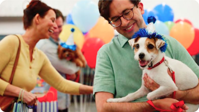 Smiling pet parents holding their dog at a birthday party with festive decorations