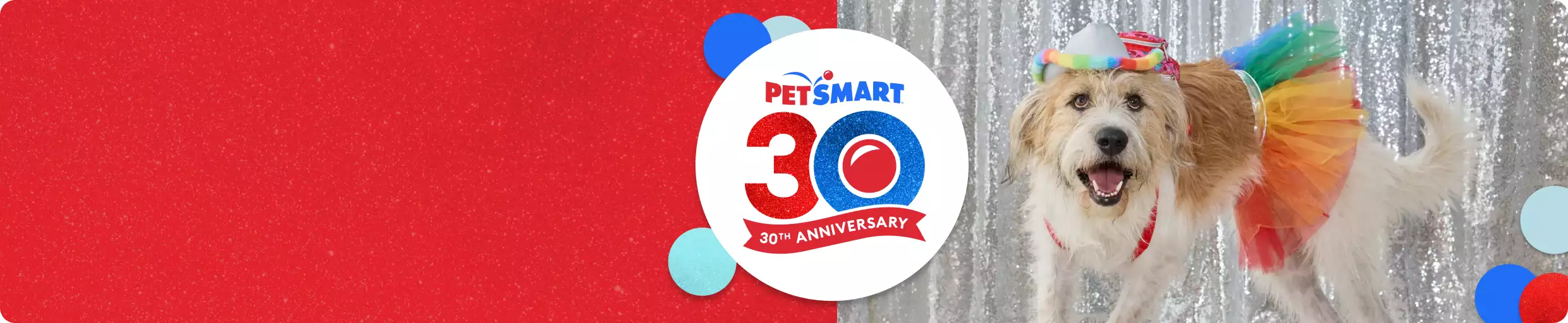 Dog wearing a rainbow tutu & headband in front of a silver backdrop & a PetSmart 30th anniversary logo