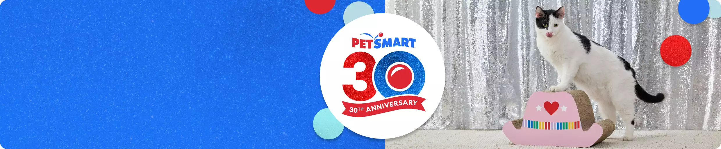 Black & white cat standing on a pink cowboy hat scratcher in front of a silver backdrop & PetSmart 30th anniversary logo
