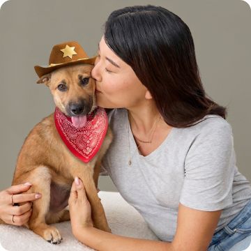 Woman kissing dog wearing a cowboy costume