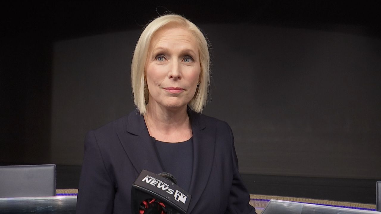 A woman wearing a black shirt and a black blazer stands in front of a black Spectrum News NY1 microphone.