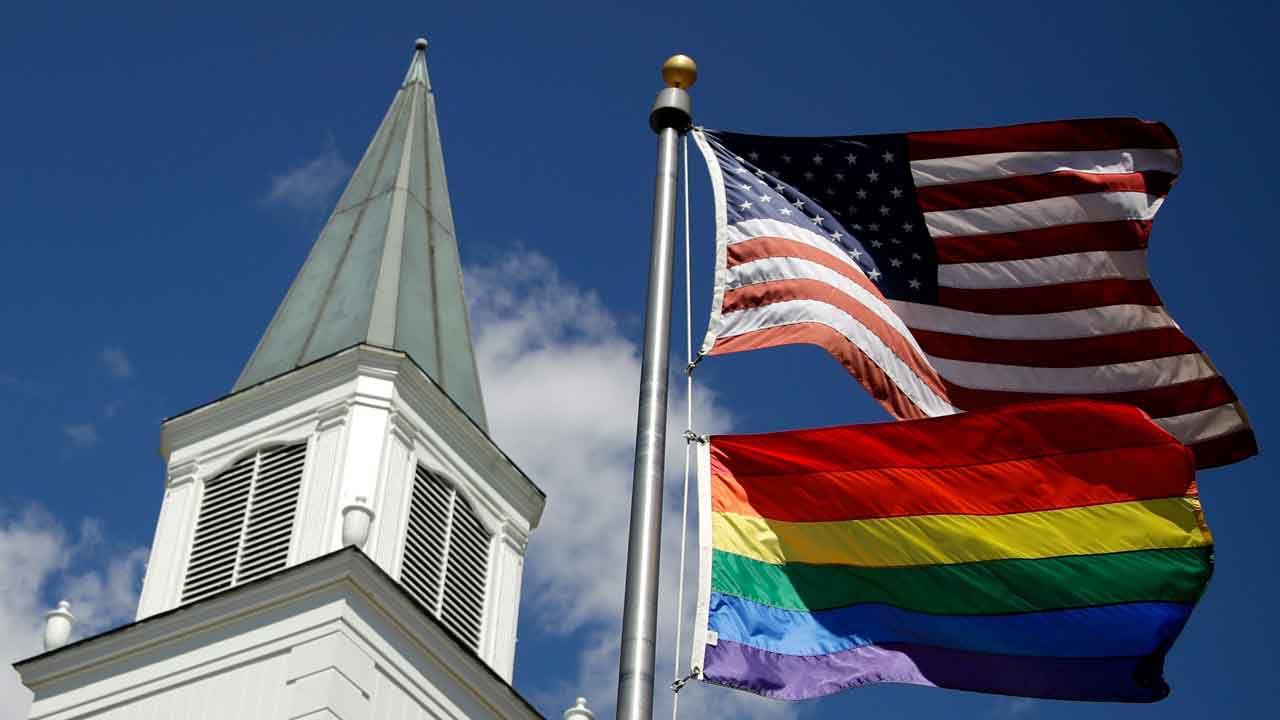 A gay pride rainbow flag flies along with the U.S. flag in front of the Asbury United Methodist Church in Prairie Village, Kan., on Friday, April 19, 2019. (AP Photo/Charlie Riedel)