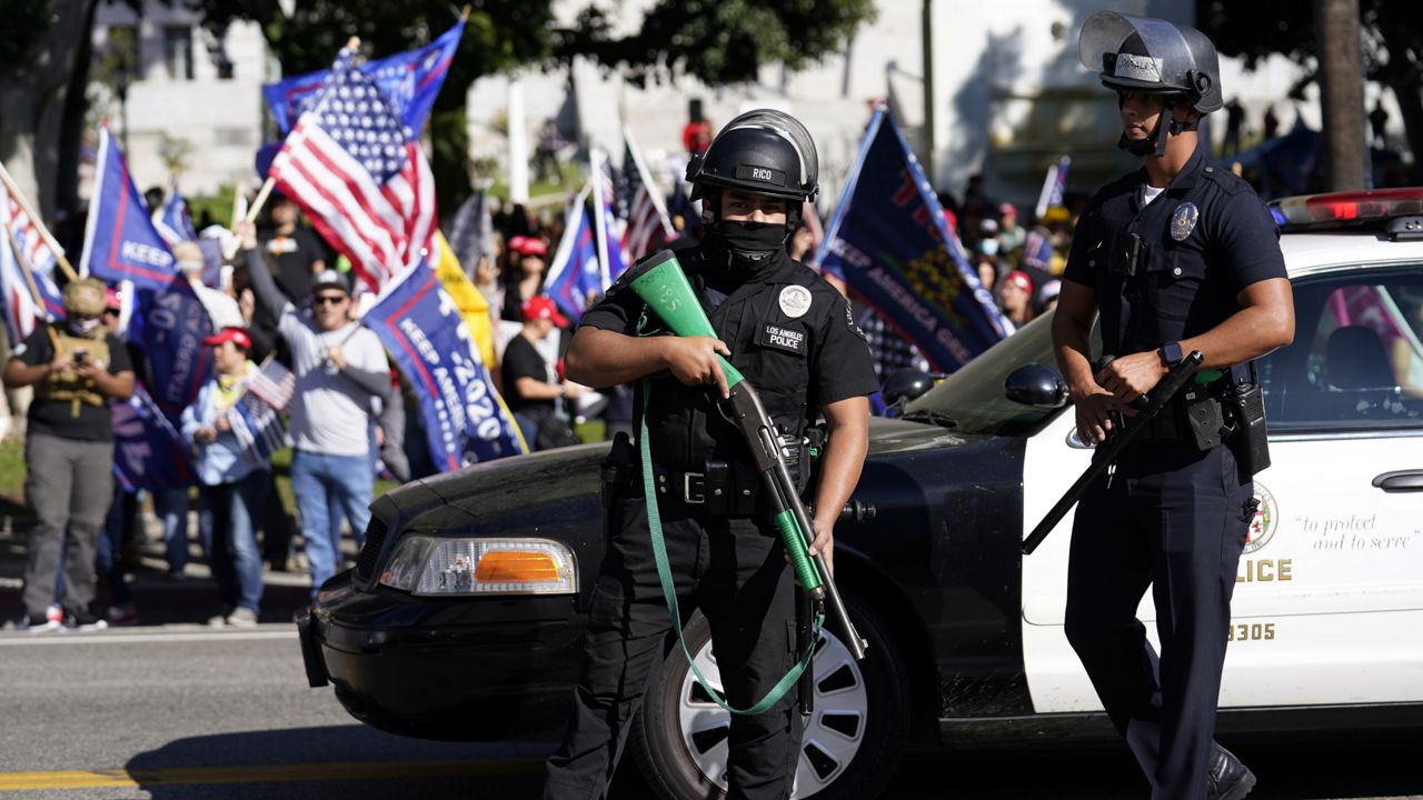Police officers hold weapons in front of a crowd of President Donald Trump supporters outside of City Hall Wednesday, Jan. 6, 2021, in Los Angeles. (AP Photo/Marcio Jose Sanchez)