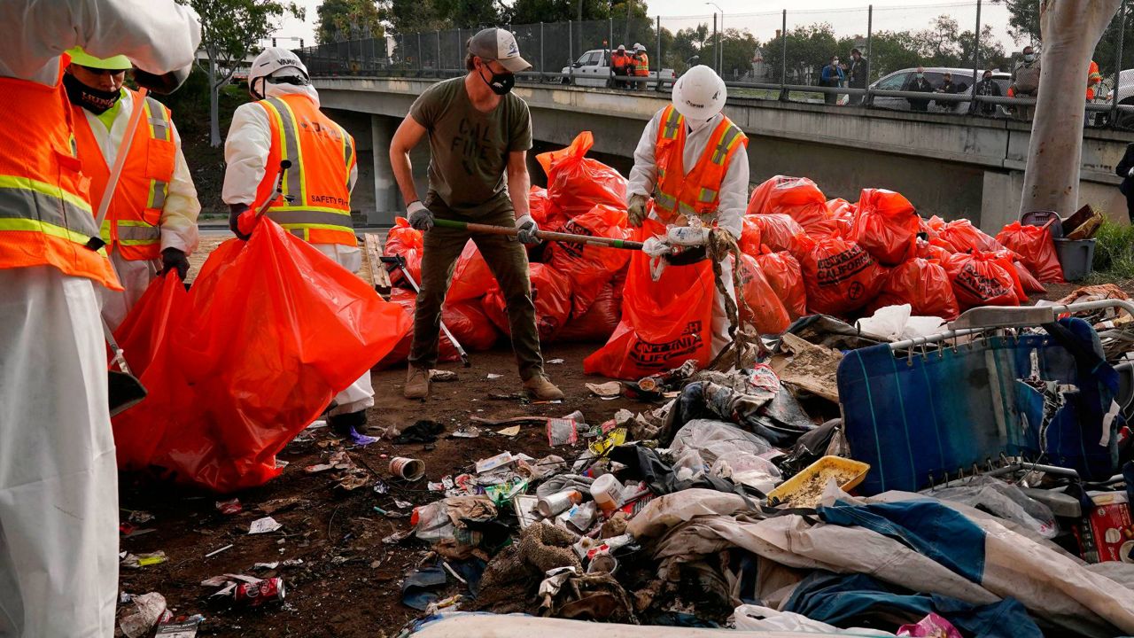 California Gov. Gavin Newsom, center, helps clean a homeless encampment alongside a freeway on Jan. 12, 2022, in San Diego. (AP Photo/Gregory Bull, File)