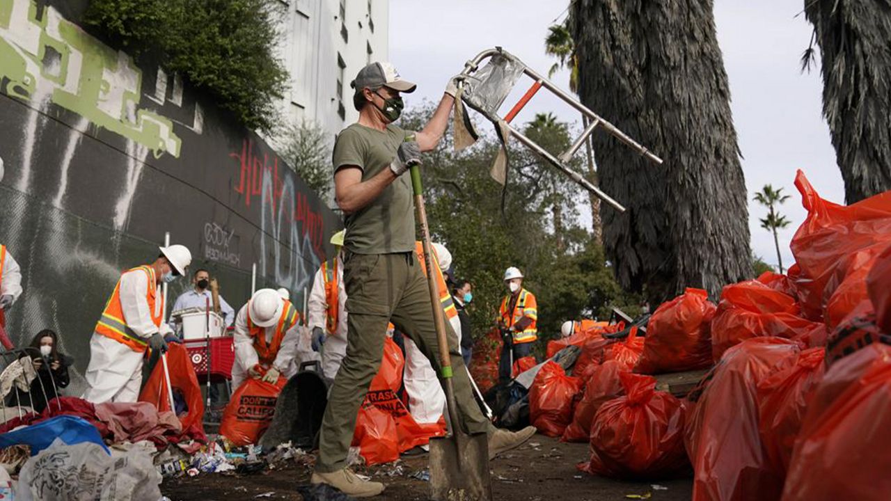 California Gov. Gavin Newsom, center, helps clean a homeless encampment alongside a freeway, Wednesday, Jan. 12, 2022, in San Diego. Newsom is calling for $2 billion to expand access to housing and mental health services for homeless people. (AP Photo/Gregory Bull)