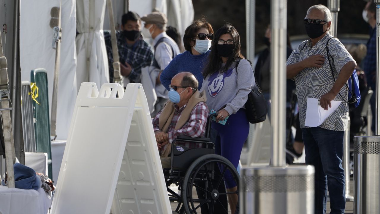 Orange County residents wait in line outside tents for a COVID-19 vaccine at the Toy Story parking lot at the Disneyland Resort Wednesday, Jan. 13, 2021, in Anaheim, Calif. (AP Photo/Damian Dovarganes)