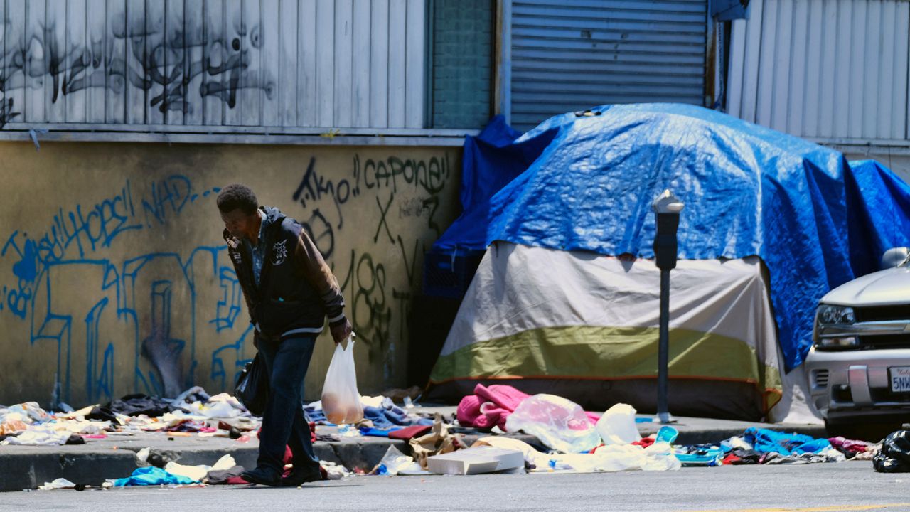 In this May 30, 2019, file photo, a homeless man walks along a street lined with trash in downtown Los Angeles. (AP Photo/Richard Vogel, File)