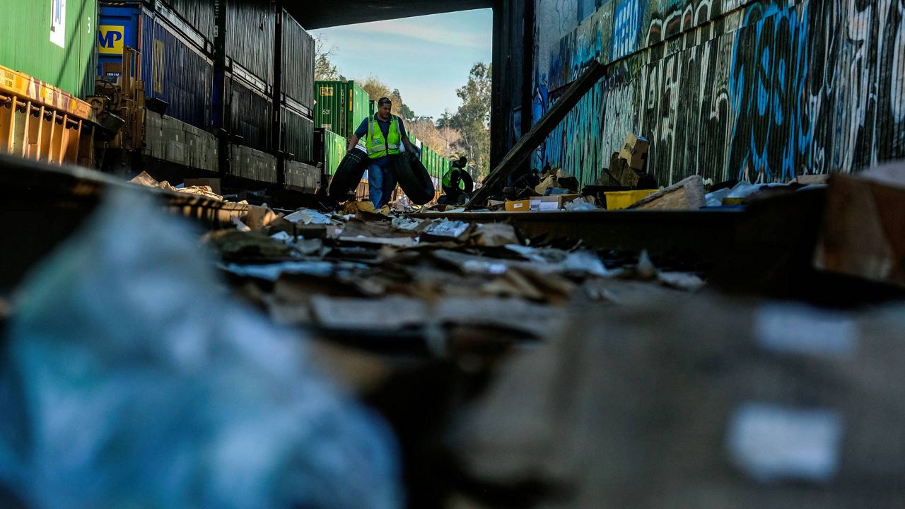 Contractor workers Adam Rodriguez, front, and Luis Rosas pick up vehicle tires from the shredded boxes and packages along a section of the Union Pacific train tracks in downtown Los Angeles on Friday. (AP Photo/Ringo H.W. Chiu)