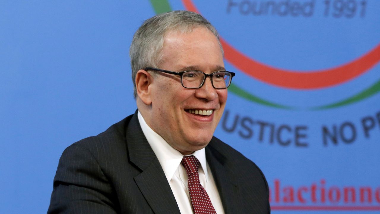 New York City Comptroller Scott Stringer, wearing black, square-framed glasses, a black suit jacket, a white dress shirt, and a scarlet tie with white spots, sits in a front of a blue background at the National Action Network House of Justice in Manhattan.