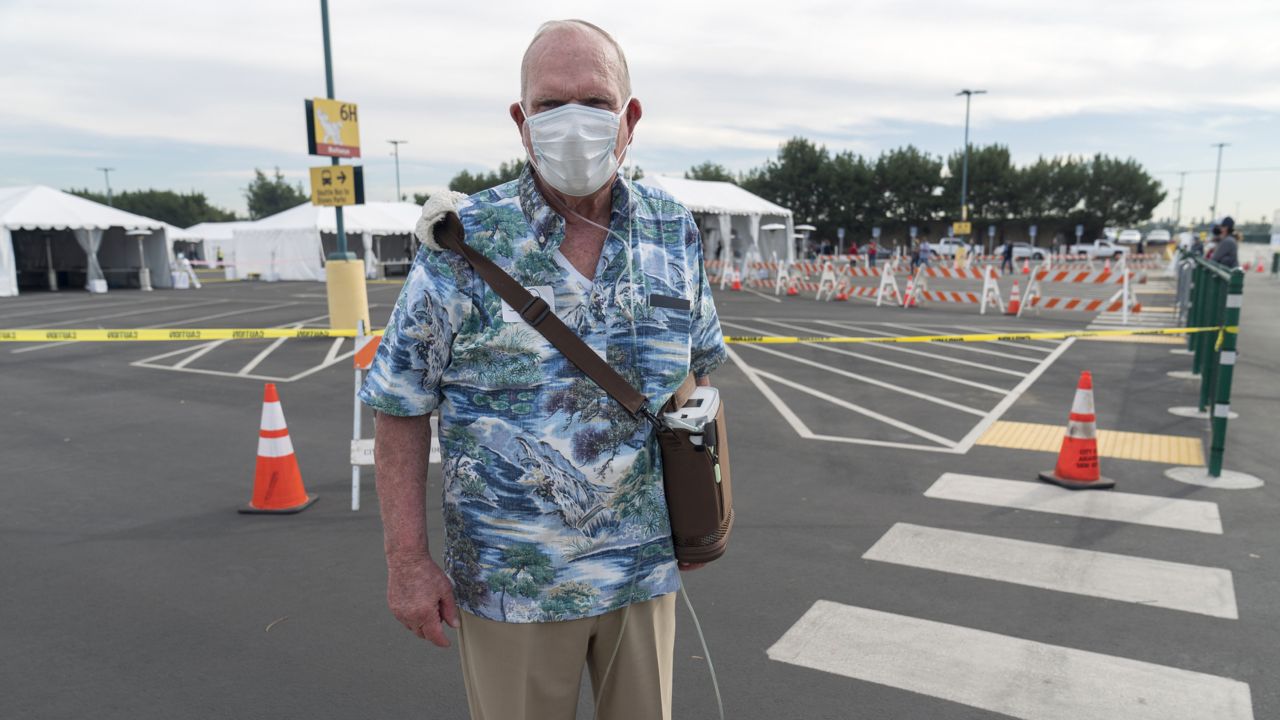 Gary Dohman, 81, from San Clemente Calif., who suffers from lung cancer, walks with an Oxygen machine, after getting a vaccine at the Disneyland Resort serving as a Super POD (Point Of Dispensing) COVID-19 mass vaccination site Wednesday, Jan. 13, 2021, in Anaheim, Calif. (AP Photo/Damian Dovarganes)