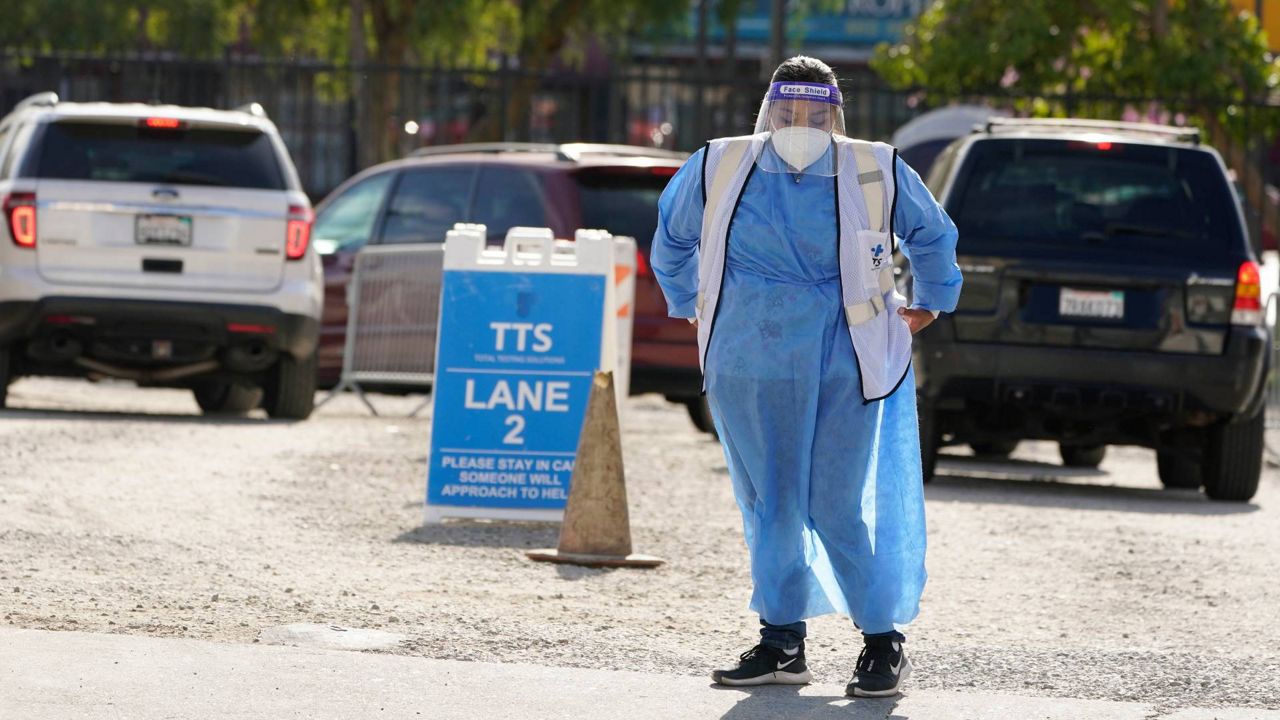 A worker stands in front of a line of vehicles at a COVID-19 testing site, Wednesday, Jan. 26, 2022, in the Boyle Heights section of Los Angeles. (AP Photo/Marcio Jose Sanchez, File)