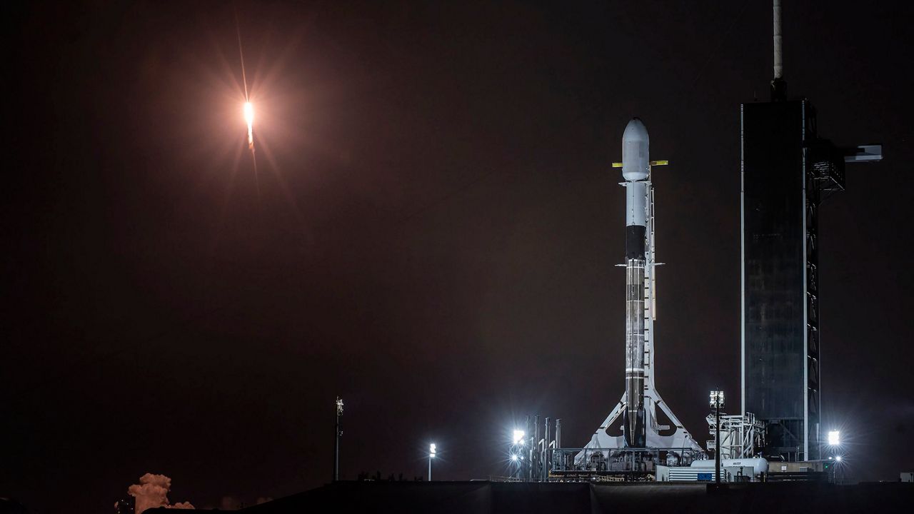 A SpaceX Falcon 9 rocket sits on Pad 39A as it waits for its Sunday launch. In the background, another SpaceX Falcon 9 rocket takes off as it sends Starlink satellites into orbit on Thursday, February 4, 2021. (SpaceX)