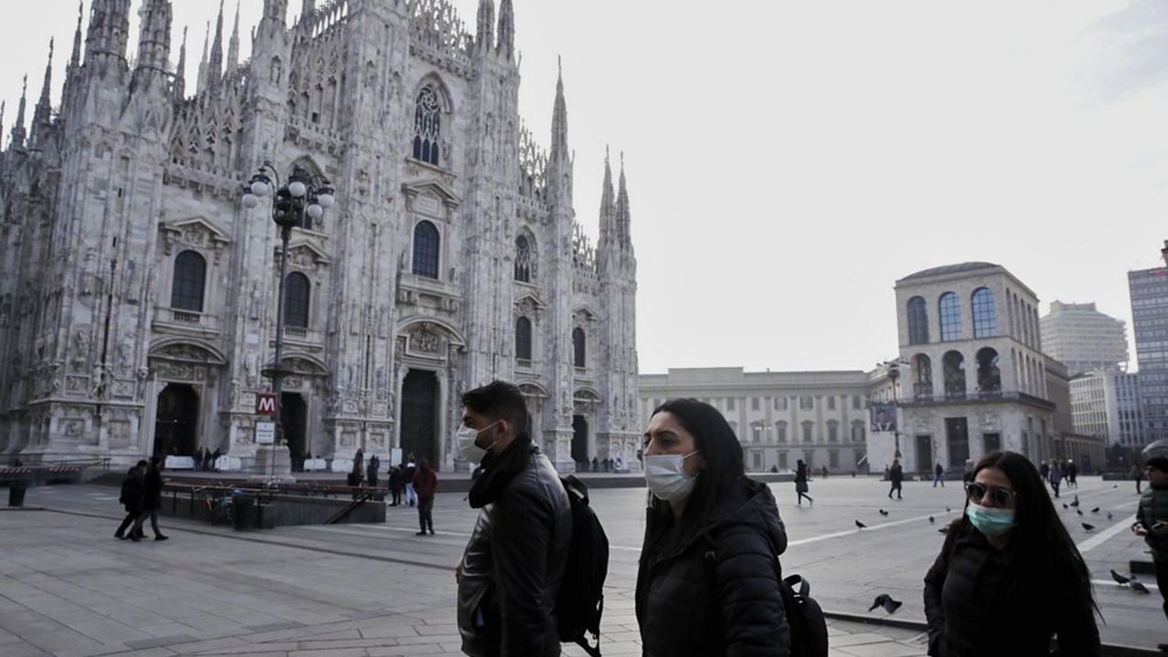 People wearing sanitary masks walk past the Duomo gothic cathedral in Milan, Italy, Sunday, Feb. 23, 2020. A dozen Italian towns saw daily life disrupted after the deaths of two people infected with the virus from China and a pair of case clusters without direct links to the outbreak abroad. A rapid spike in infections prompted authorities in the northern Lombardy and Veneto regions to close schools, businesses and restaurants and to cancel sporting events and Masses. (AP Photo/Luca Bruno)