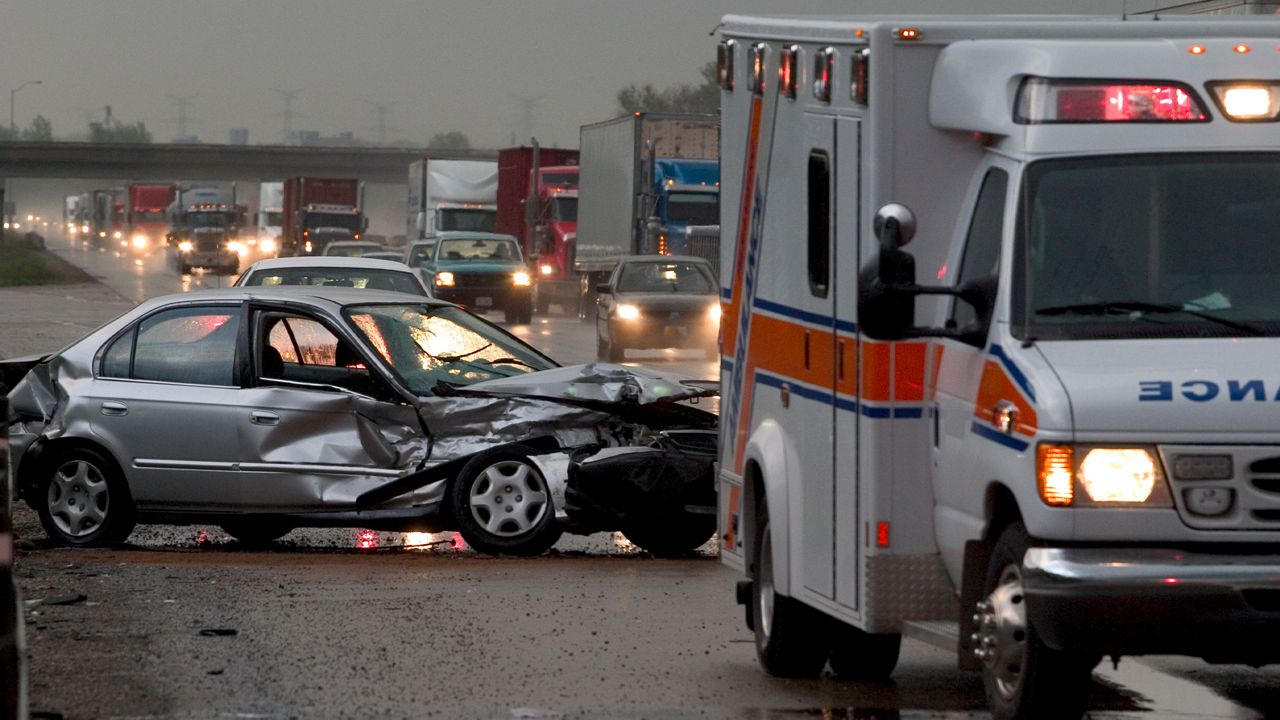 Car crash on major highway during rainfall at night. Ambulance in foreground and police car in background.