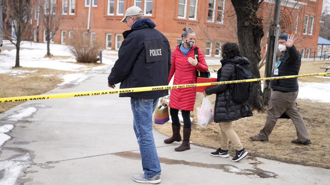 Police officer escorts people past a police line in front of University Hill Elementary School across from the campus of the University of Colorado after a man accused of making mass shooting threats against the college as well as the University of California, Los Angeles, was arrested Tuesday, Feb. 1, 2022, in Boulder, Colo. (AP Photo/David Zalubowski)