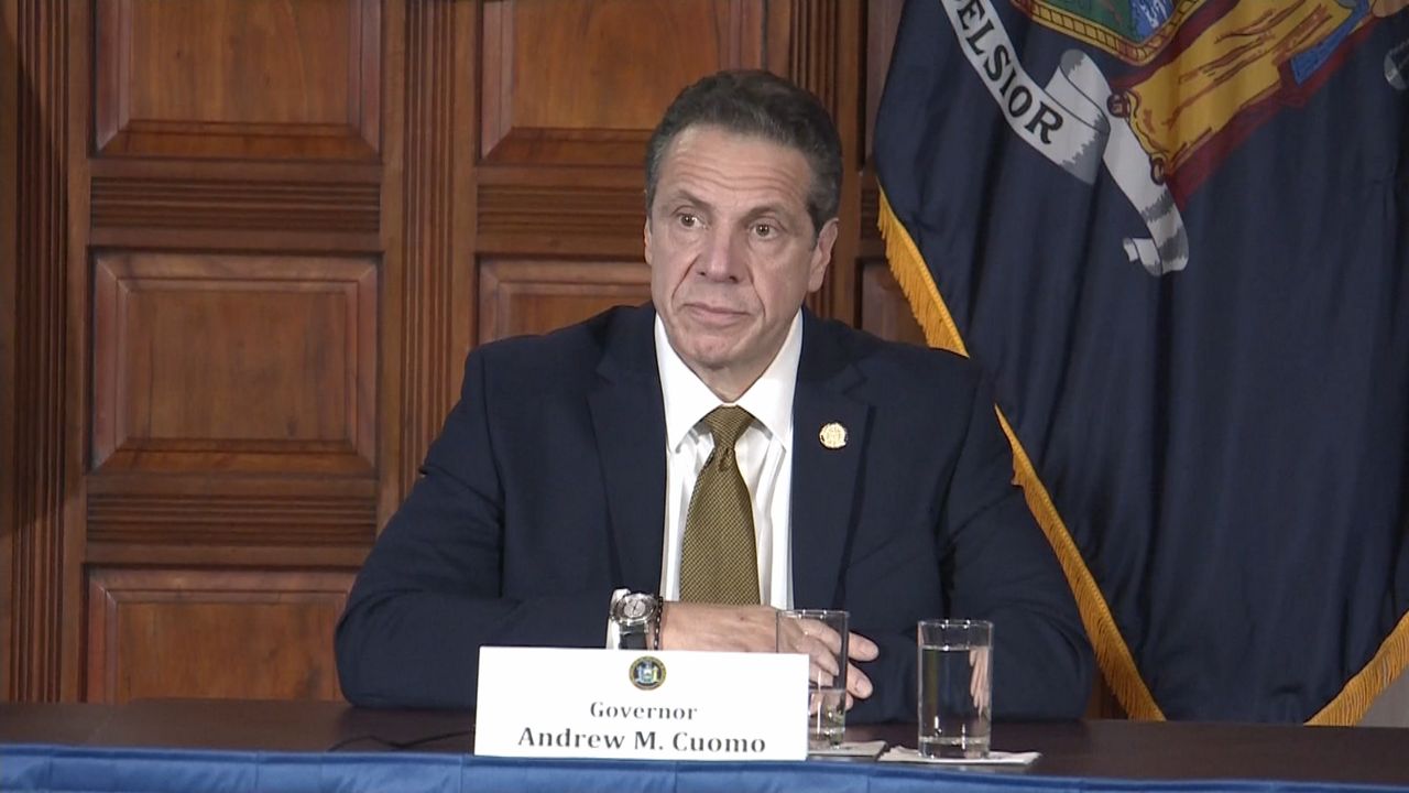 Andrew Cuomo, wearing a green tie, a white dress shirt, and a black suit jacket.