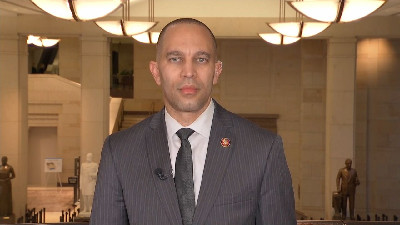 Rep. Hakeem Jeffries of the 8th Congressional District in New York, wearing a grey suit jacket, a white dress shirt, and a black tie, stands in a hall in the U.S. Capitol.