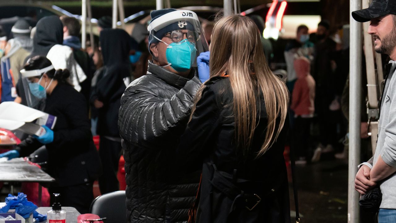 Clinical assistant Richard Wrangel, center left, collects a nasal swab sample from a hockey fan for a COVID-19 test in the parking lot of the Honda Center before an NHL hockey game between the Anaheim Ducks and the Vancouver Canucks, Wednesday, Dec. 29, 2021, in Anaheim, Calif. (AP Photo/Jae C. Hong)