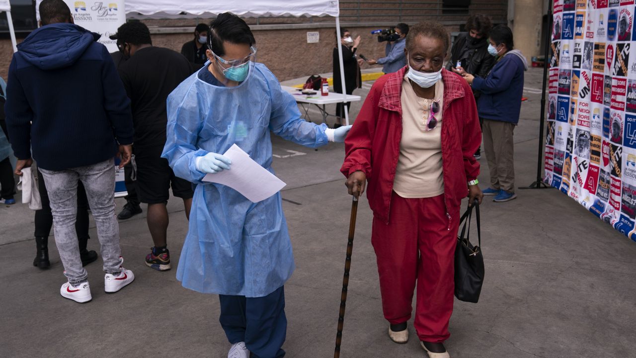 Vera Eskridge, 86, right, is escorted into the waiting area by registered nurse Angelo Bautista after getting her COVID-19 vaccine at a vaccination site set up in the parking lot of the Los Angeles Mission in the Skid Row area of Los Angeles, Wednesday, Feb. 10, 2021. (AP Photo/Jae C. Hong)