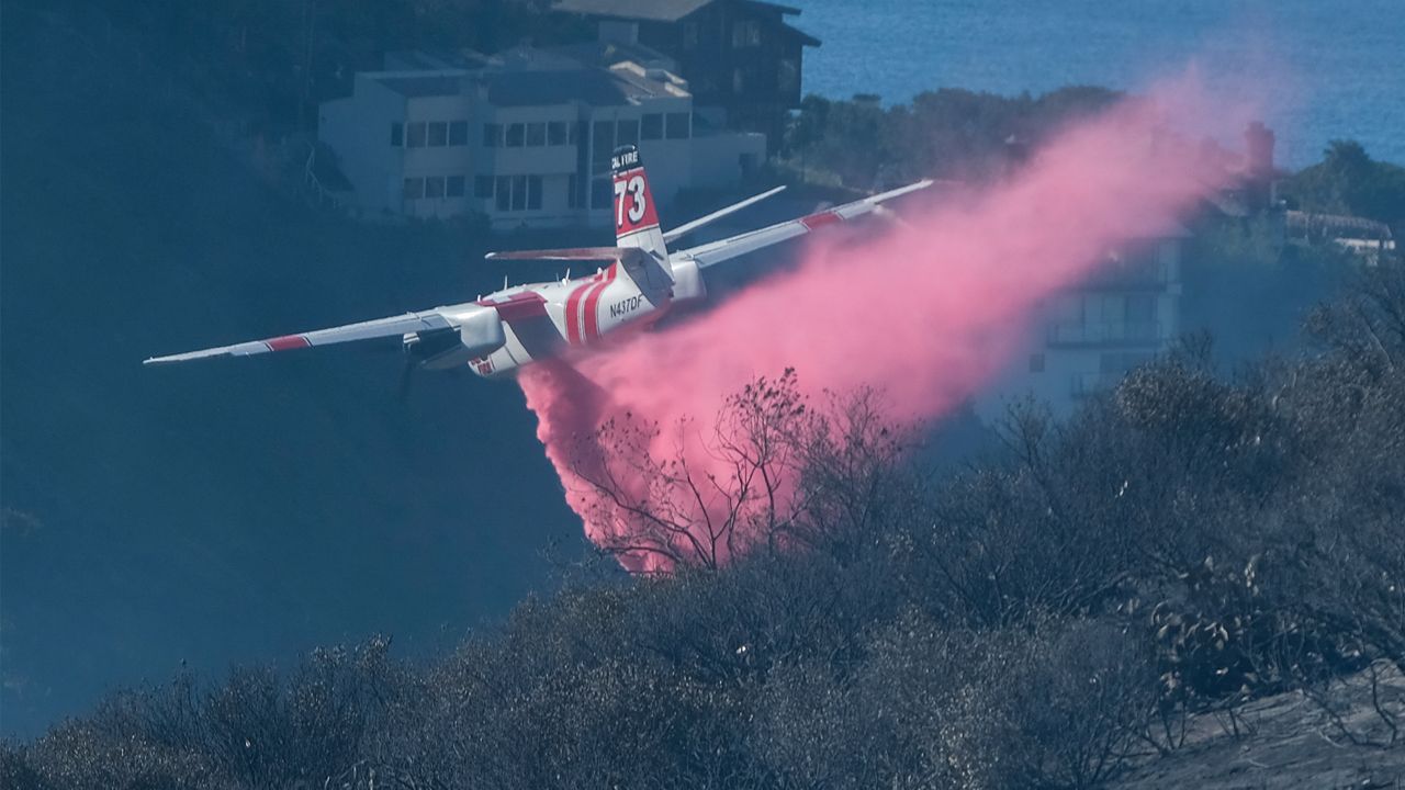 A plane drops retardant on a wildfire near homes Thursday, Feb. 10, 2022, in Laguna Beach, Calif. (AP Photo/Ringo H.W. Chiu)