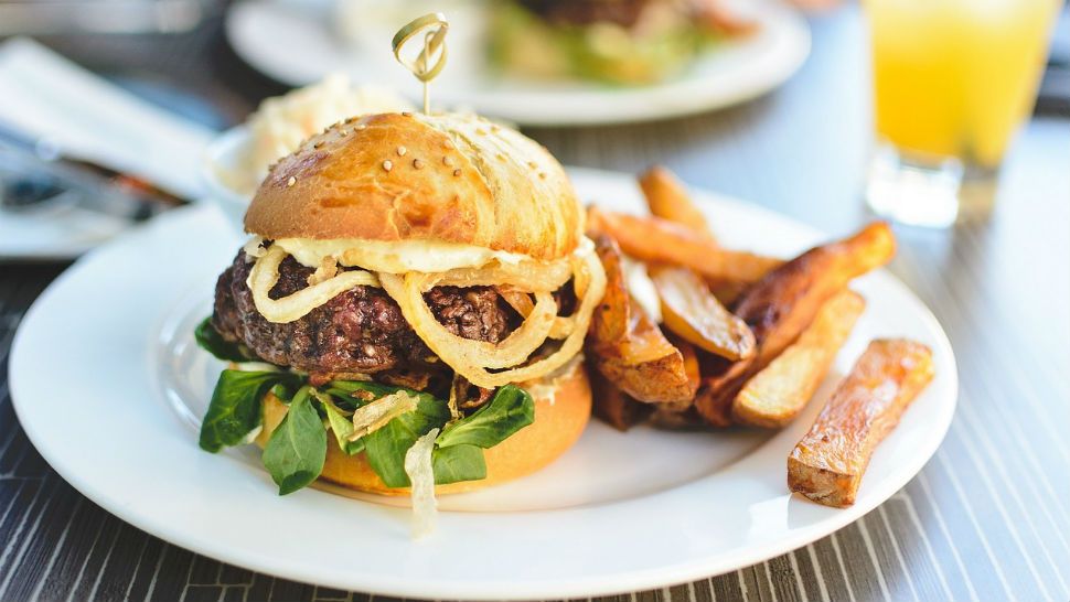 A burger served on a bed of greens, with caramelized onions, toasted sesame bun and steak fries. (Pixabay)