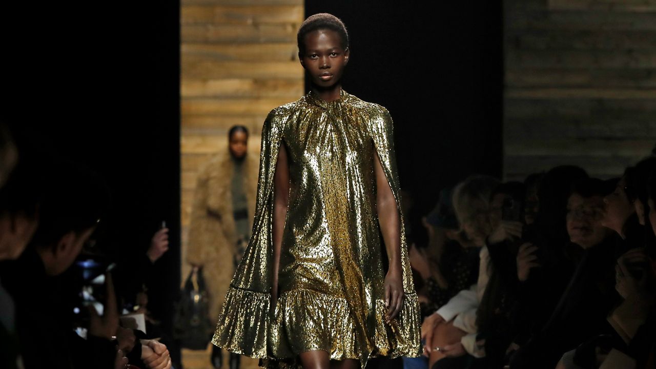 A woman wearing a gold dress walks the runway at New York Fashion Week for the Michael Kors collection.