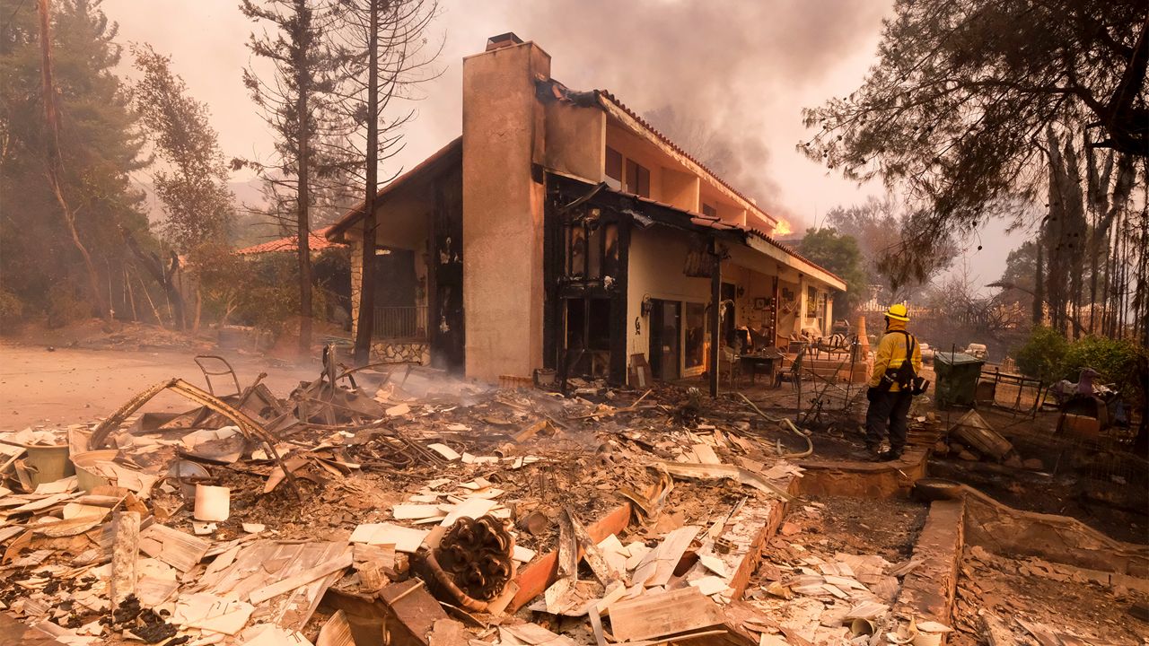 In this Nov. 9, 2018, file photo, a firefighter keeps watch as the charred remains of a burned out home are seen during the Woolsey Fire in Malibu, Calif. (AP Photo/Ringo H.W. Chiu, File)